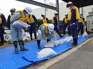 ヘルメットを被った消防隊員と作業員がブルーシートの上に土のうを置いている写真