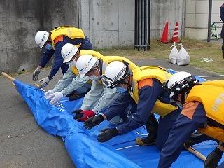 ヘルメットを被った消防隊員と作業員がブルーシートを敷いている写真