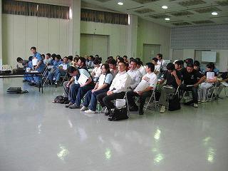 多数の人が広い部屋で椅子に座って市民救命士講習会に参加している写真