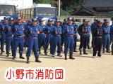 青い服を着た「小野市消防団」の人たちがバスの前に集まっている写真