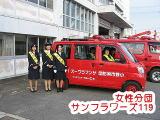 赤い車の後方で3人の女性分団サンフラワーズ119の隊員が並んでいる写真