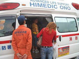 オレンジ色の服を着た消防隊員に見守られて救急車に人が乗り込んでいる写真