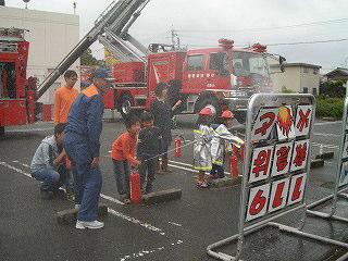 消防隊員の見守る中で男の子が水消火器を使って的に当てている写真
