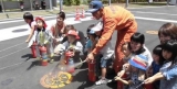 子どもたちが消火器を使って消火訓練をするのを消防隊員が指導している写真