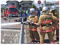 3人の防護服を着た消防隊員が放水訓練をしている写真