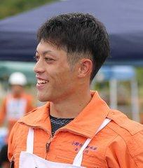 オレンジ色の消防士の制服を着て、左側を向いて笑顔を見せている様子の長谷川 滉一さんの写真