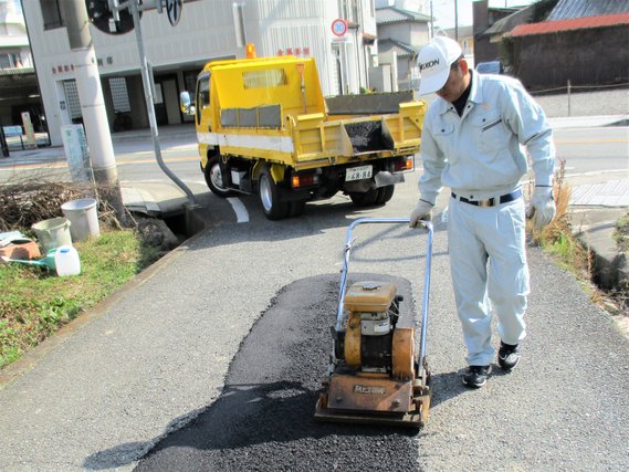 グレー上下のユニファーム姿で白い帽子を被った作業員がアスファルトの工事をしている写真