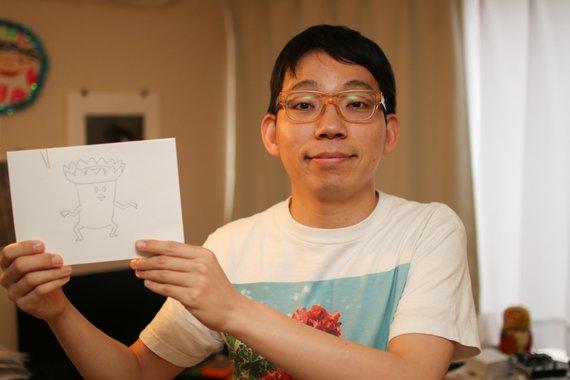 メガネを書けた男性が制作アニメのキャラクターを掲げている写真