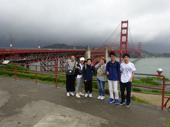 赤い橋を背景に団員が6人並んでいる記念写真